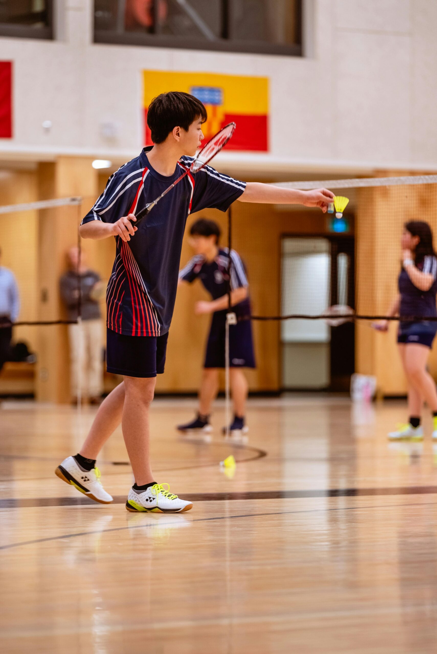Teenagers engaged in a game of badminton indoors, showcasing teamwork and sportsmanship.