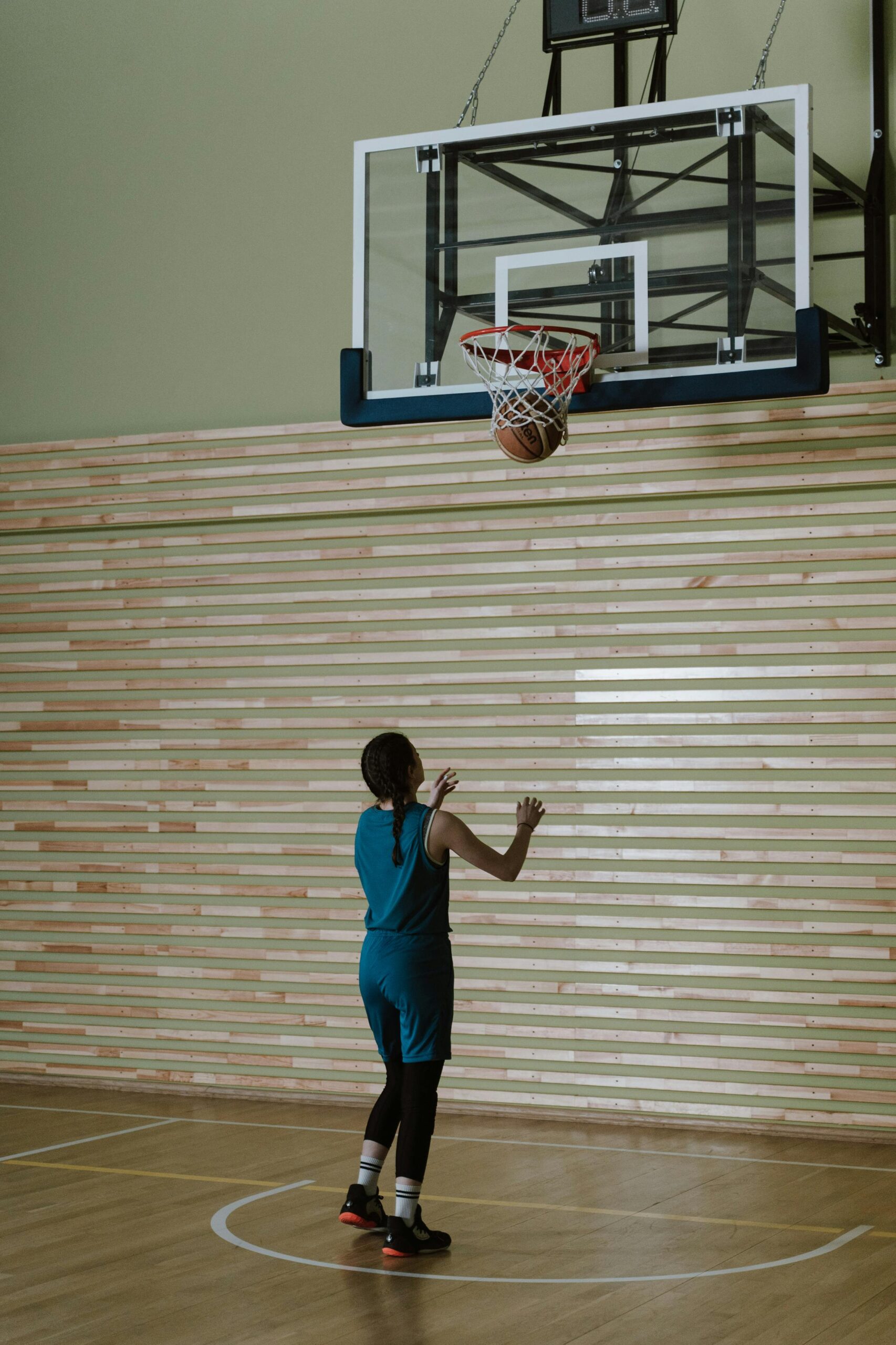 A teenager practicing basketball indoors, focusing on shooting hoops.
